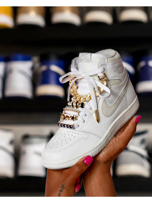 White sneaker with gold and silver lace charms and lace tips for sneakers held in hand.