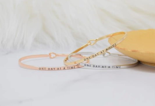 Inspirational "One Day at a Time" bangle bracelets in gold, silver, and rose gold, perfect for stacking and gifting.